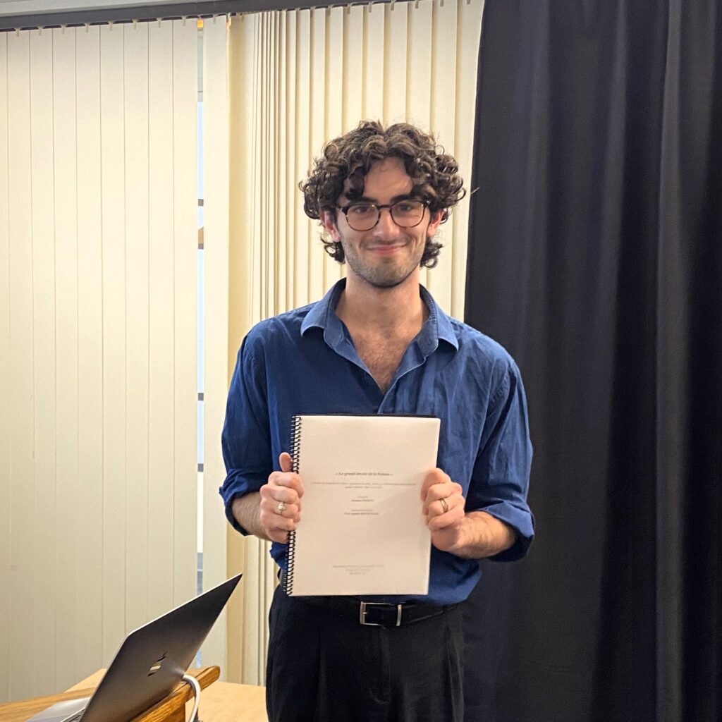young man smiling and holding thesis book