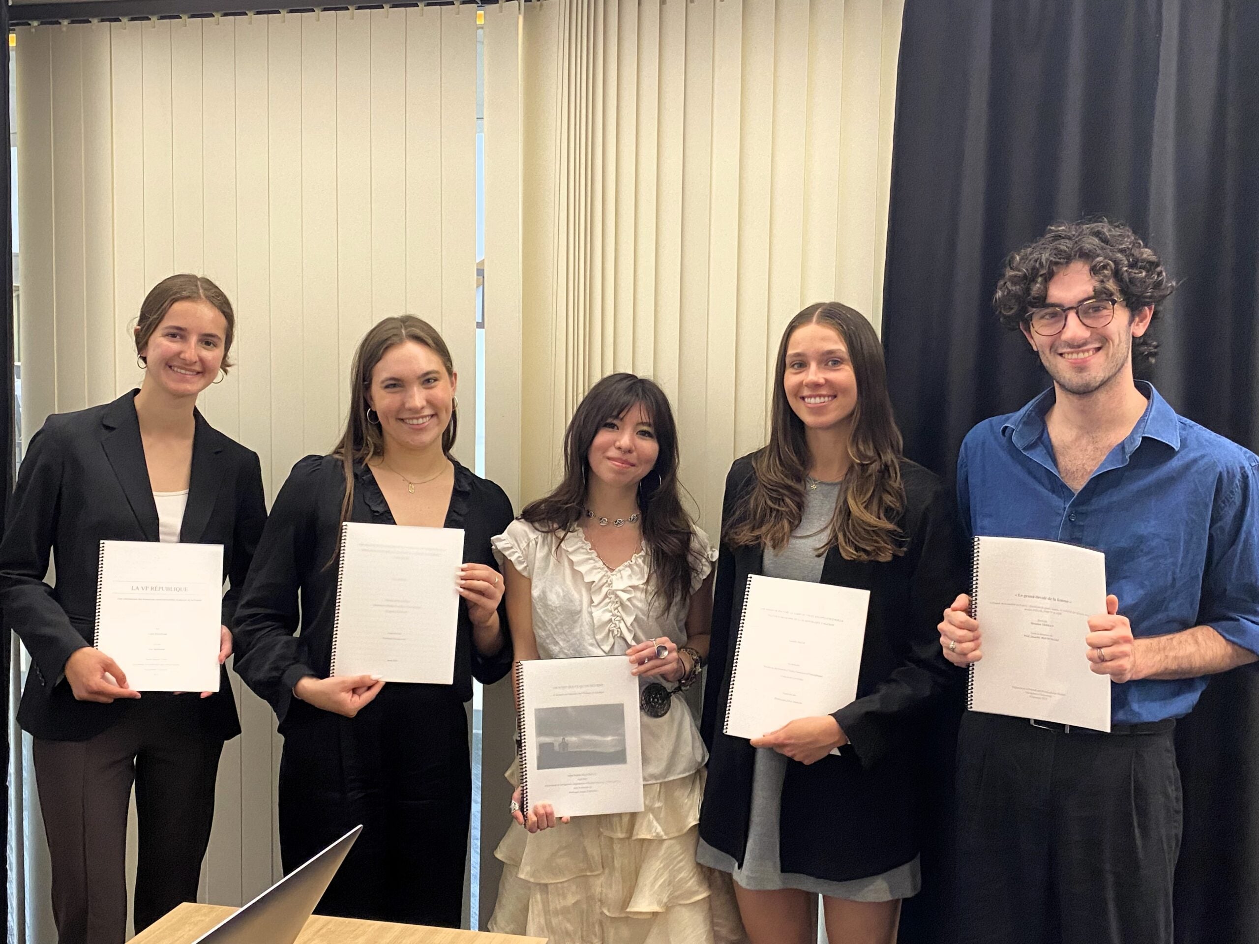 five students holding thesis books in front of them