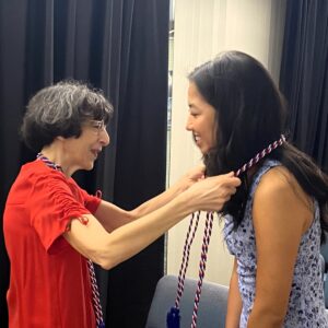 woman placing red, white, and blue cords around neck of young woman