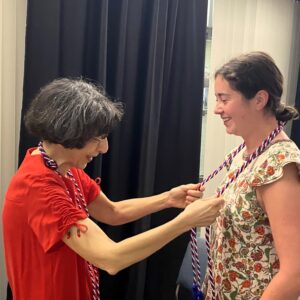 woman placing red, white, and blue cords around neck of young woman